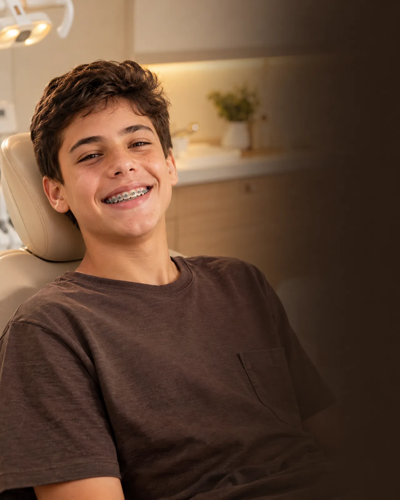 Menino de treze anos sorrindo com aparelho fixo, na cadeira odontológica