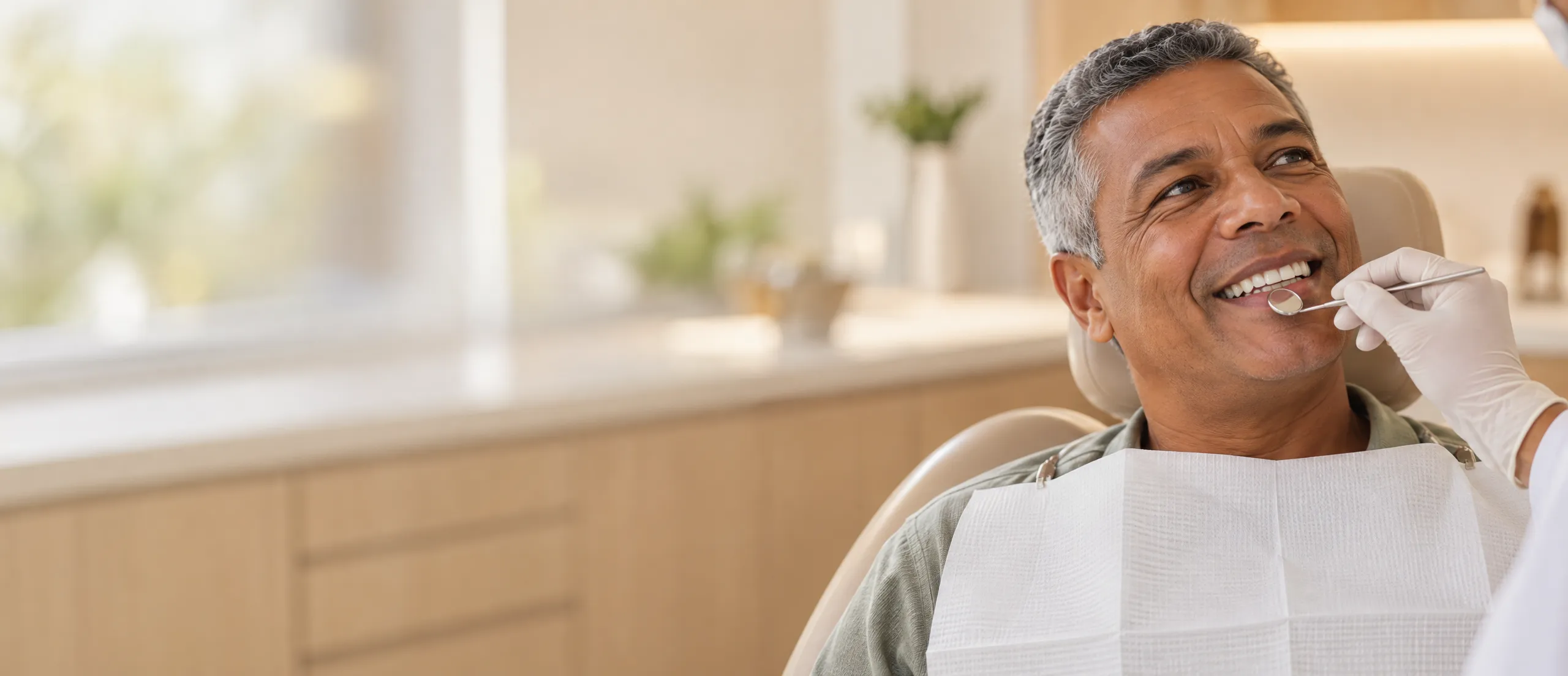 Paciente sorrindo na cadeira enquanto o espelho odontológico mostra a linha da gengiva
