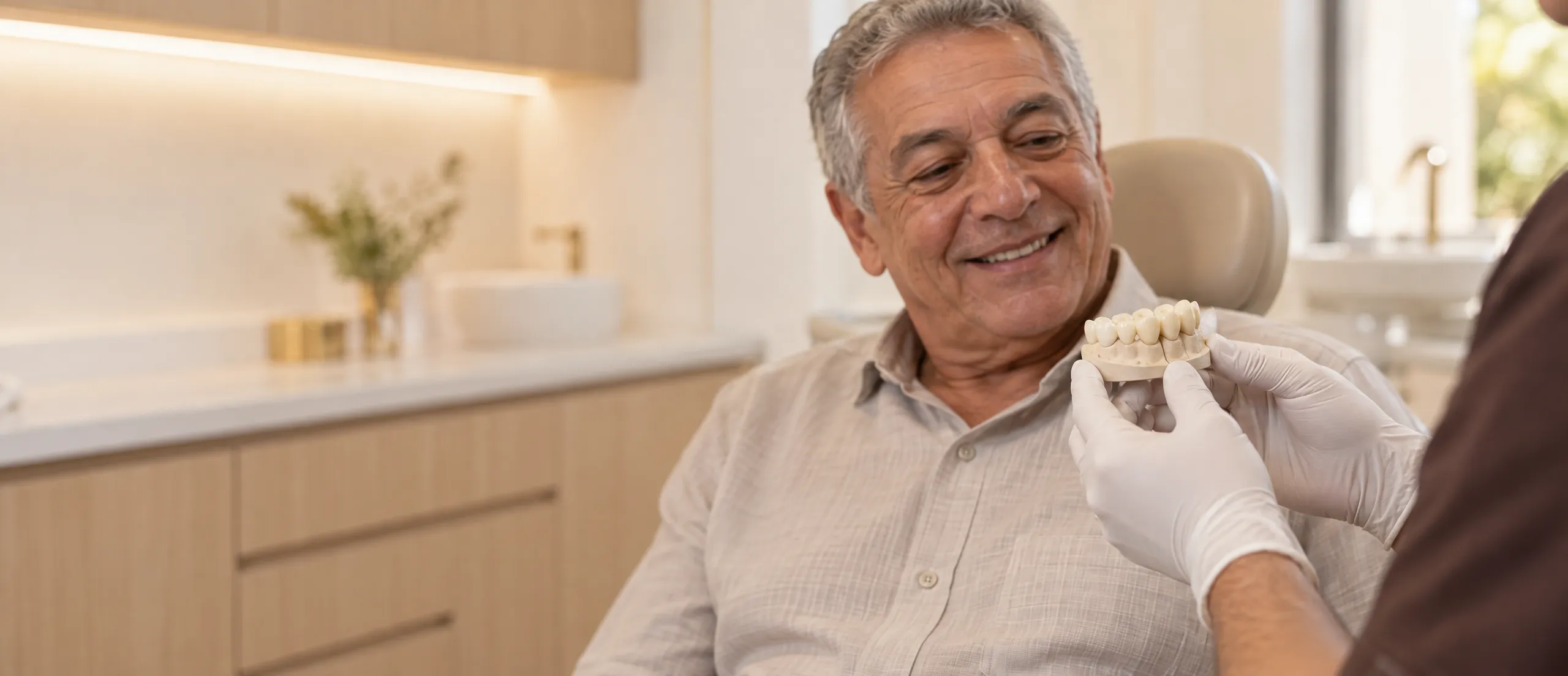 Mãos enluvadas apresentam uma prótese dentária a um paciente na cadeira odontológica