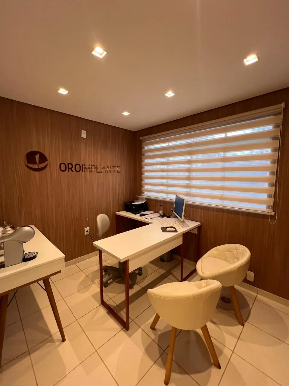 Sala de avaliação da OroImplante, com mesa, poltronas claras e parede de madeira com o logo